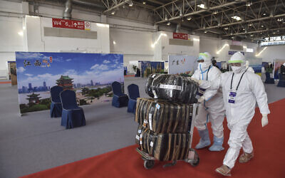 Illustrative: In this March 17, 2020 photo released by China's Xinhua News Agency, workers in protective suits push a cart with passengers' luggage at the New China International Exhibition Center, which has been converted into a facility to screen international flight passengers arriving in Beijing.  (Peng Ziyang/Xinhua via AP)