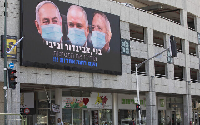 A billboard shows Israeli Prime Minister Benjamin Netanyahu, left, Avigdor Liberman, center, and Blue and White party leader Benny Gantz, wearing masks in the Israeli city of Ramat Gan on March 29, 2020. The text urges them to take off the masks, because "the people want unity." (AP/Sebastian Scheiner)