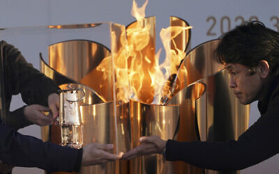 In this March 25, 2020, file, photo, officials light a lantern from the Olympic Flame at the end of a flame display ceremony in Iwaki, northern Japan. (AP/Eugene Hoshiko)
