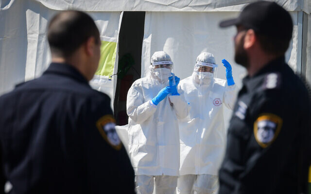 Magen David Adom medical team members, wearing protective gear, handle a coronavirus test sample at a drive-through site for testing in Tel Aviv, on March 22, 2020. (Flash90)