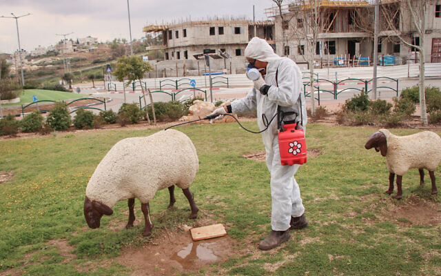 A worker in protective clothing disinfects a public playground in the West Bank settlement of Efrat on March 22, 2020. (Gershon Elinson/Flash90)