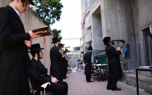 Ultra-Orthodox Jewish men pray outside a closed yeshiva, in the town of Bnei Brak, on March 26, 2020. (Tomer Neuberg/Flash90)