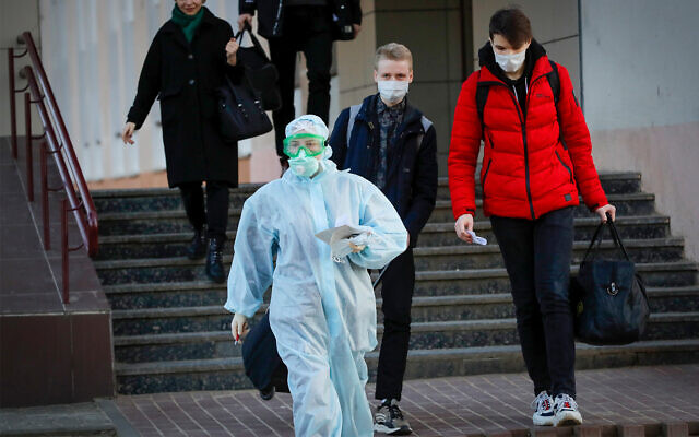 A medical worker wearing a protective suit assists students to an ambulance in Minsk, Belarus, March 13, 2020. (AP Photo/Sergei Grits)