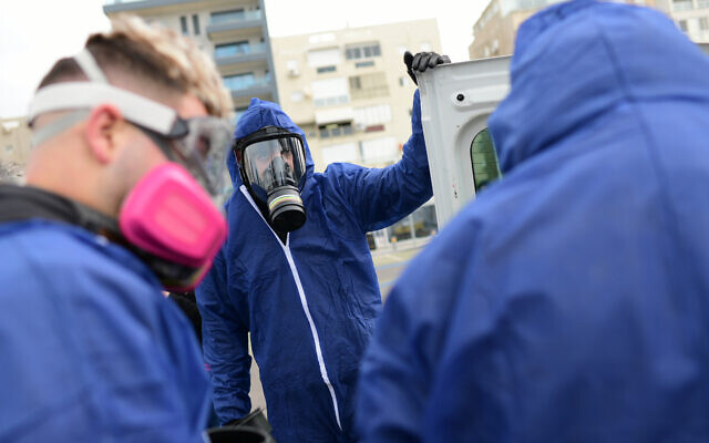 Workers wearing protective clothes disinfect a public playground in Bat Yam as part of measures to prevent the spread of the Coronavirus, March 18, 2020. (Tomer Neuberg/Flash90)