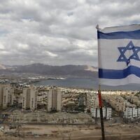 An Israeli flag flutters as the Red Sea resort city of Eilat and Jordan's Red Sea resort city of Aqaba are seen in the background, on April 17, 2020. (Menahem Kahana/AFP)