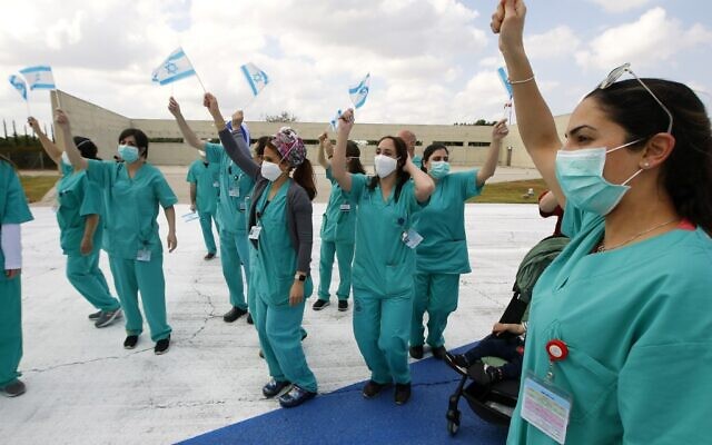Staff at Sheba Medical Center at Tel HaShomer wave national flags as the Israeli Air Force aerobatic team fly over the hospital during Israel's Independence day celebrations in a salute to medical teams fighting the coronavirus outbreak, April 29, 2020. (JACK GUEZ/AFP)