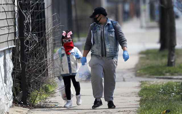 In this April 7, 2020 photo, Erica Harris, right, and her daughter Jordan, wear their protective masks as they walk back home after getting a lunch and homework from the child’s school on Chicago’s Southside in Chicago (AP Photo/Charles Rex Arbogast)