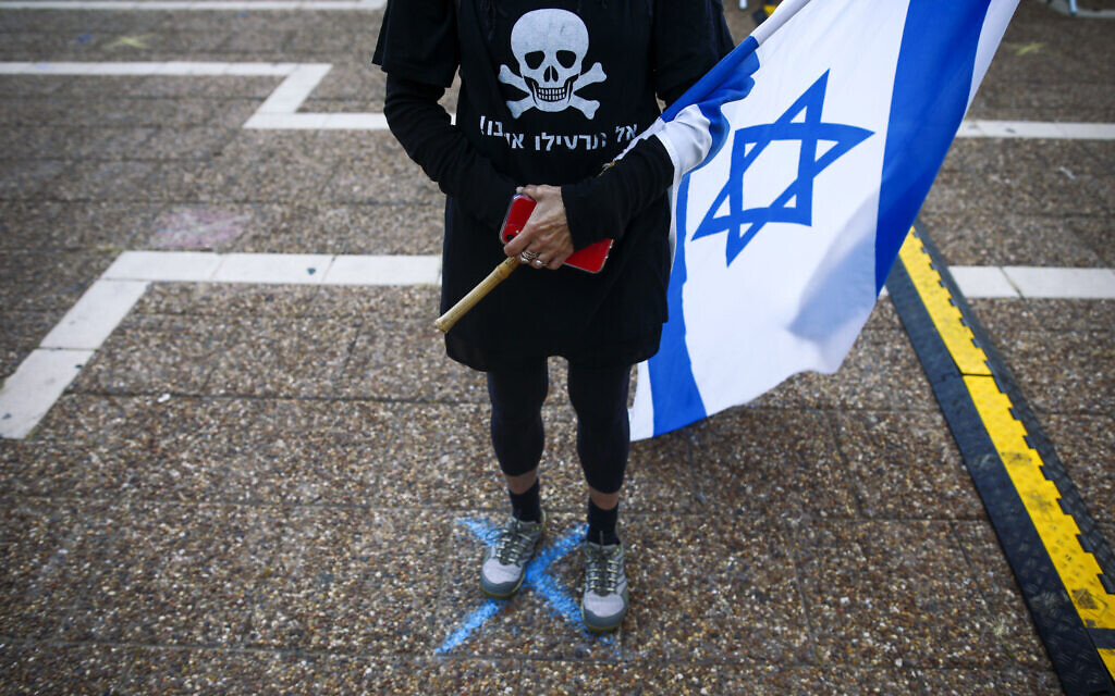In this Saturday, April 25, 2020 photo, a woman stands on a spot marked with "X'" spaced over two meters apart in order for people to keep social distancing amid concerns over the country's coronavirus outbreak, during "Black Flag" protest against Prime Minister Benjamin Netanyahu and government corruption, at Rabin Square in Tel Aviv, Israel. (AP Photo/Oded Balilty)