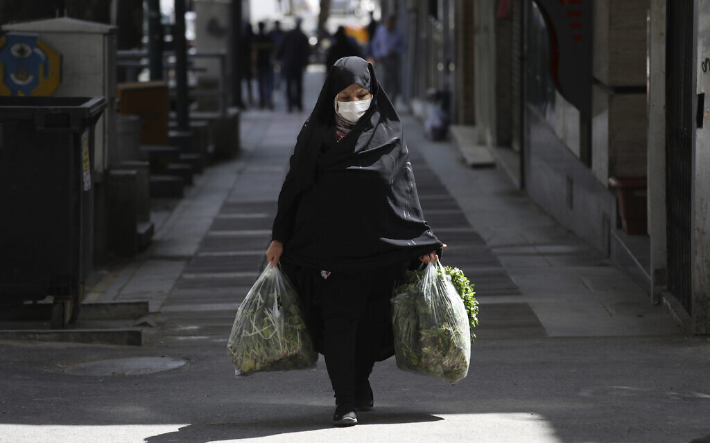 A woman wearing a face mask to protect against the new coronavirus carries her shopping in northern Tehran, Iran, Saturday, April 4, 2020. (AP Photo/Vahid Salemi)
