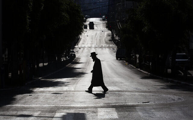 An ultra-Orthodox Jew crosses a mainly deserted street because of the government's measures to help stop the spread of the coronavirus, in Bnei Brak, Israel, Wednesday, April 8, 2020. (AP Photo/Oded Balilty)