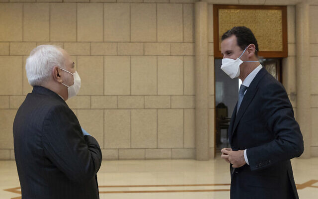Syrian President Bashar Assad, right, wears a mask to help protect from the coronavirus, as he speaks with Iranian Foreign Minister Mohammad Javad Zarif, who also wore a mask and gloves, in Damascus, Syria, April. 20, 2020. (SANA via AP)