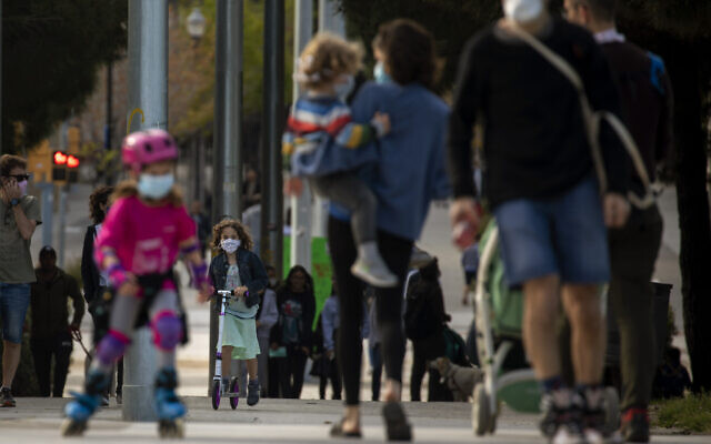 Families with their children walk along a boulevard in Barcelona, Spain, Sunday, April 26, 2020 as the lockdown to combat the spread of coronavirus continues. From Sunday, children under 14 years old will be allowed to take walks with a parent for up to one hour and within one kilometer from home, ending six weeks of compete seclusion. (AP Photo/Emilio Morenatti)