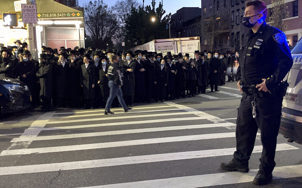 A New York City police officer keeps watch as hundreds of mourners gather in the Brooklyn borough of New York, Tuesday, April 28, 2020, to observe a funeral for Rabbi Chaim Mertz, a Hasidic Orthodox leader whose death was reportedly tied to the coronavirus.(Peter Gerber via AP)