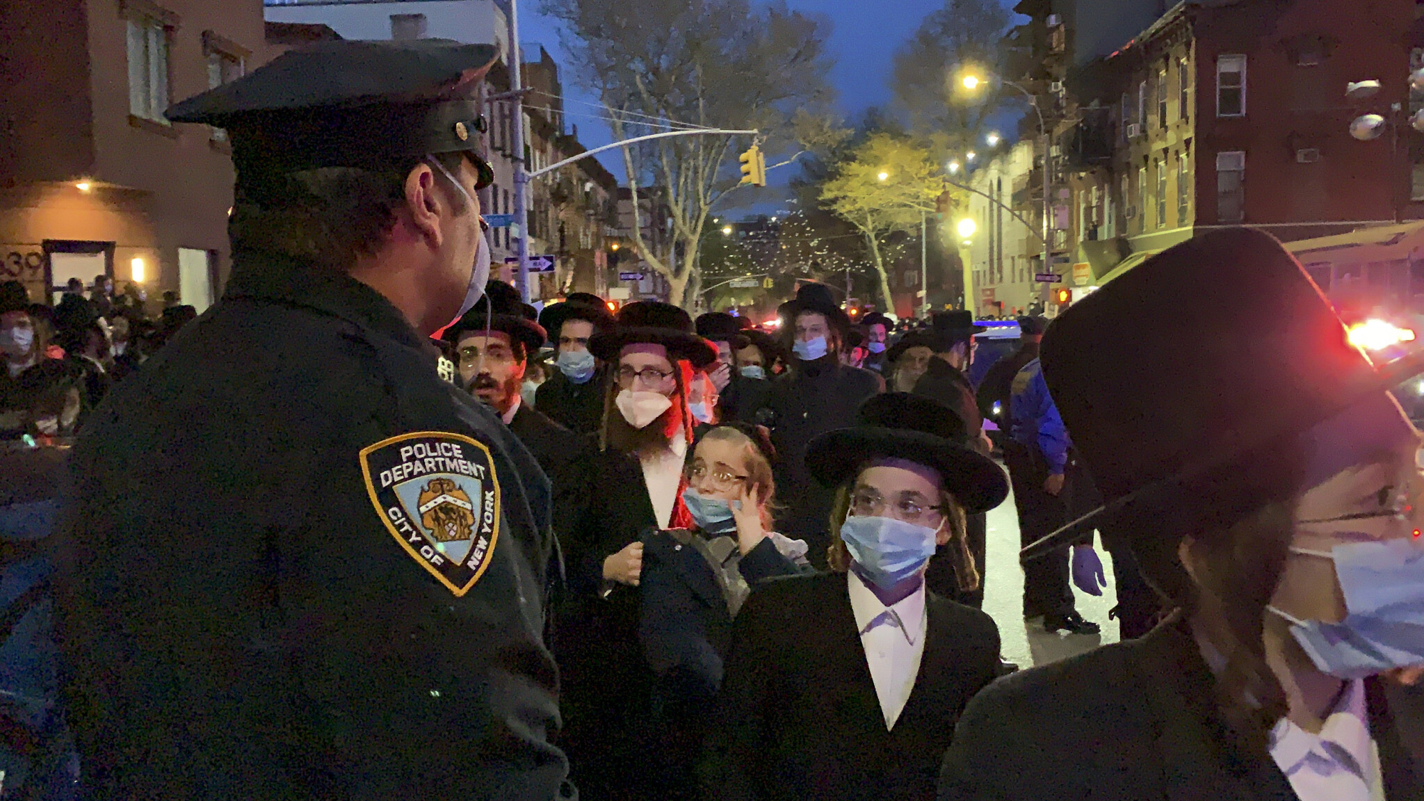 A New York City police officer keeps watch as hundreds of mourners gather in the Brooklyn borough of New York, Tuesday, April 28, 2020, to observe a funeral for Rabbi Chaim Mertz, a Hasidic Orthodox leader whose death was reportedly tied to the coronavirus. (Peter Gerber via AP)