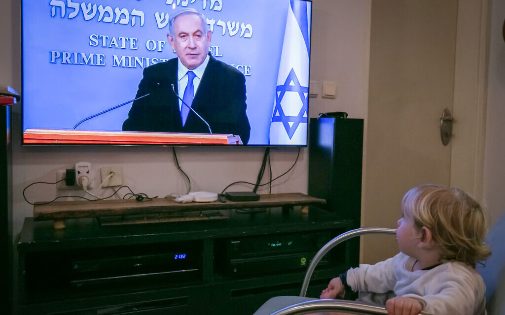 An Israeli child watch as Israeli prime minister Benjamin Netanyahu holds a live press conference on the new government restrictions for the public regarding the coronavirus COVID-19 on March 19, 2020. (Chen Leopold/Flash90)
