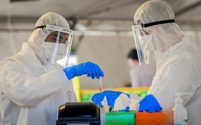 Magen David Adom medical team members, wearing protective gear, handle a coronavirus test sample at a drive-through site in Tel Aviv, March 22, 2020. (Flash90)
