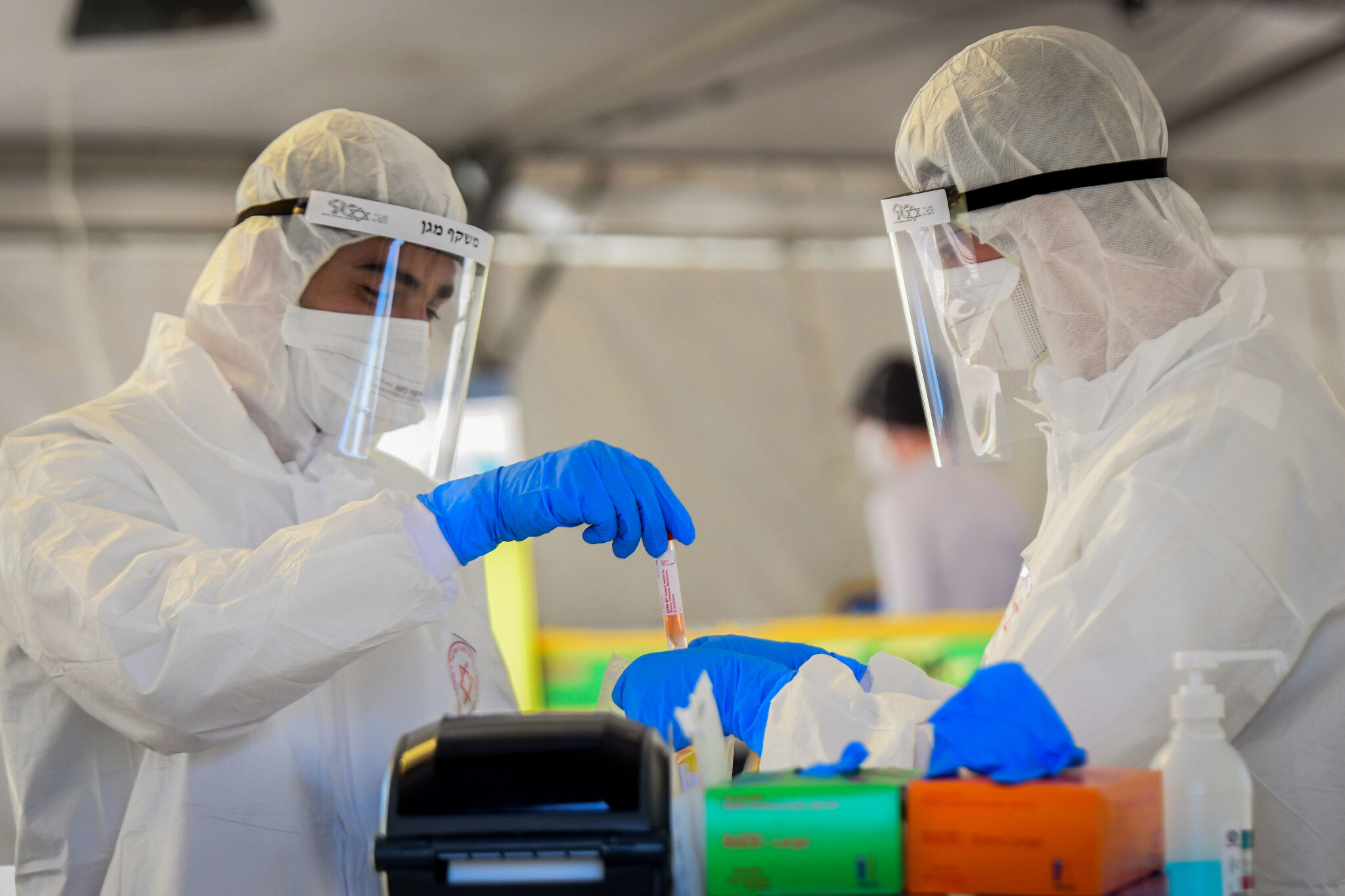 Magen David Adom medical team members, wearing protective gear, handle a coronavirus test sample at a drive-through site in Tel Aviv, March 22, 2020. (Flash90)