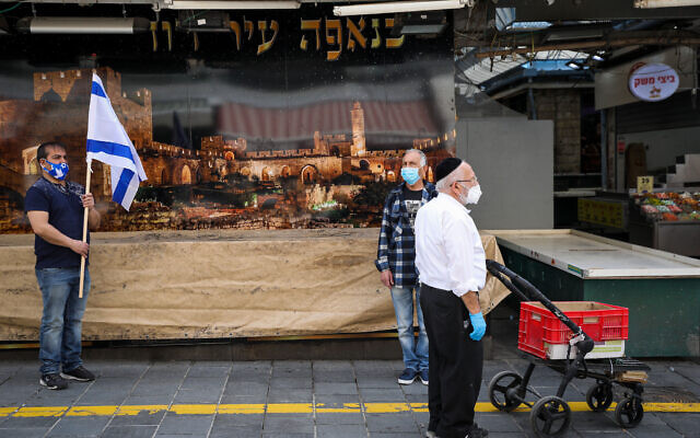 People stand still at the Mahane Yehuda Market in Jerusalem, as a two-minute siren sounds across Israel to mark Holocaust Remembrance Day on April 21, 2020 (Olivier Fitoussi/Flash90)