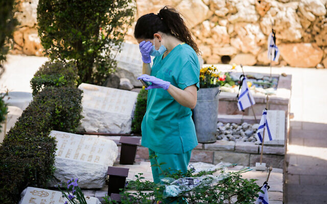 A woman in scrubs at a grave of a loved one at Mount Herzl in Jerusalem on Memorial Day on April 28, 2020. (Olivier Fitoussi/Flash90)