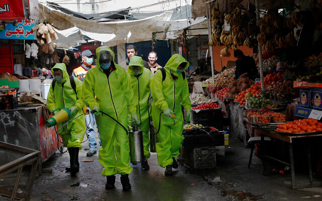 Workers wearing protective gear spray disinfectant as a precaution against the coronavirus at the main market in Gaza City, March 27, 2020. (AP/Adel Hana)