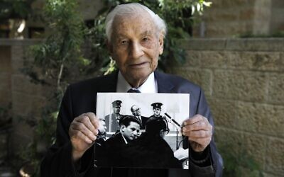 Gabriel Bach, 93, a former judge of the Supreme Court of Israel and a former deputy prosecutor during the trial of Adolf Eichmann, poses for a picture while holding a photograph showing him (below) during Eichmann's (top) trial, at the yard of his home in Jerusalem on May 3, 2020.(Photo by MENAHEM KAHANA / AFP)