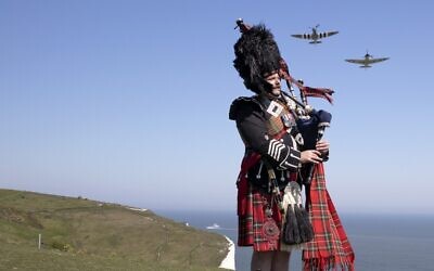 Pipe major Andy Reid of The Scots Guards plays his pipes on the cliffs of Dover, southern England on May 6, 2020 as two Spitfires from the battle of Britain memorial flight fly over him during a posed picture to commemorate the 75th anniversary of VE day (Richard Pohle / POOL / AFP)