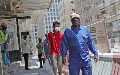 Workers wearing protective masks walk by on a street in Qatar's capital Doha, on May 17, 2020, as the country begins enforcing the world's toughest penalties for failing to wear masks in public, as it battles one of the world's highest coronavirus infection rates. (Photo by KARIM JAAFAR / AFP)