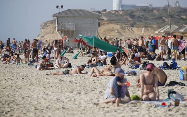 Illustrative: People lie on a beach as others cool off in the water in Netanya on May 18, 2020. (JACK GUEZ / AFP)