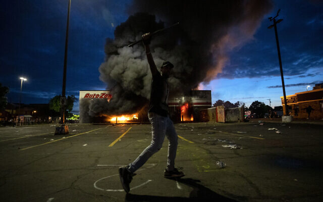 A man poses for a photo in the parking lot of an AutoZone store in flames, while protesters hold a rally for George Floyd in Minneapolis on Wednesday, May 27, 2020 (Carlos Gonzalez/Star Tribune via AP)