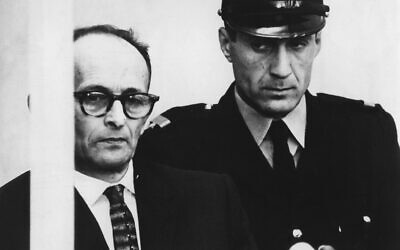 Adolf Eichmann is seen standing in his bullet proof glass box as the charges against him are read during judical proceedings in the Beit Ha'Am building in Jerusalem, April 12, 1961. (AP Photo/Str)