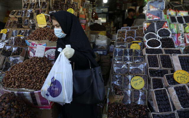 A woman wearing a protective face mask and gloves to help prevent the spread of the coronavirus carries her purchases as she leaves a store which sells dates, a favorite fruit for the Muslim holy fasting month of Ramadan, in Tehran on April 27, 2020. (AP Photo/Vahid Salemi)