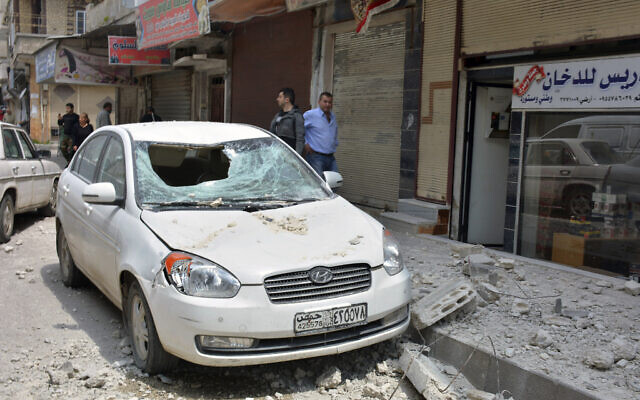 Ilustrativo: Las personas se paran cerca de un automóvil que resultó dañado debido a los escombros que volaban desde una base militar siria que albergaba un almacén de armas, en la provincia central de Homs, Siria, el 1 de mayo de 2020. (SANA, la agencia oficial de noticias siria, vía AP )