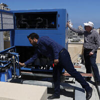 In this April 30, 2020, photo, Palestinian engineer Raed Nakhal from Palestine Children Relief Fund, right, and engineer Abdullah Dewik, check the Watergen machine that generates safe drinking water from air on the roof of al-Rantisi pediatric hospital in Gaza City. (AP Photo/Adel Hana)