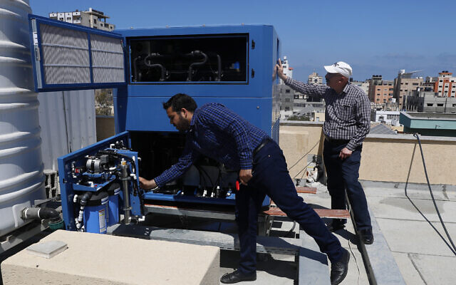 In this April 30, 2020, photo, Palestinian engineer Raed Nakhal from Palestine Children Relief Fund, right, and engineer Abdullah Dewik, check the GEN-M machine that generates safe drinking water from air at the roof of al-Rantisi pediatric hospital in Gaza City. (AP Photo/Adel Hana)