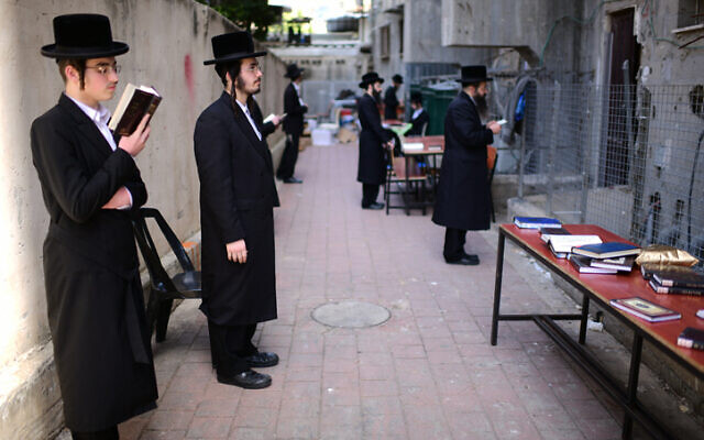 Ultra-Orthodox Jewish men pray outside a closed yeshiva in Bnei Brak on March 26, 2020. (Tomer Neuberg/Flash90)