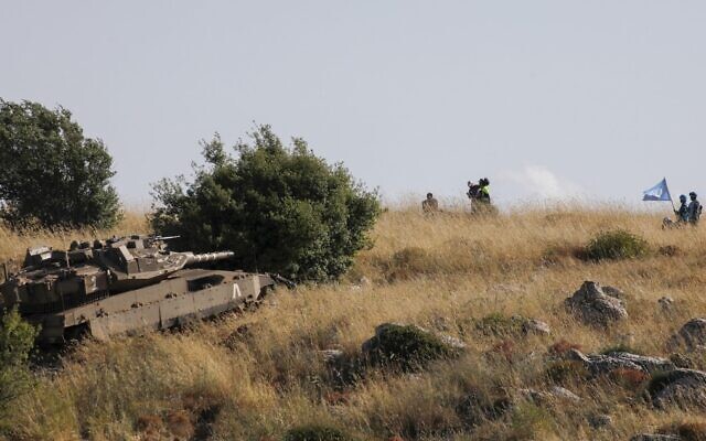 In this photo taken near Kibbutz Misgav Am, Lebanese soldiers and UNIFIL peacekeepers watch from the southern Lebanese village of Adaisseh as an IDF Merkava tank takes part in routine maneuvers near the border demarcation line, June 2, 2020. (Jalaa Marey/AFP)