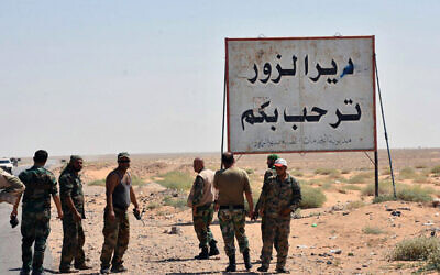This file photo released Sept. 3, 2017, by the Syrian official news agency SANA, shows Syrian troops and pro-government gunmen standing next to a sign in Arabic which reads, "Deir el-Zour welcomes you," in the eastern city of Deir el-Zour, Syria. (SANA via AP)