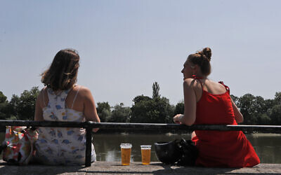 Two women sit with take away drinks from a pub on the banks of the river Thames in London, Tuesday, June 23, 2020. (AP/Frank Augstein)