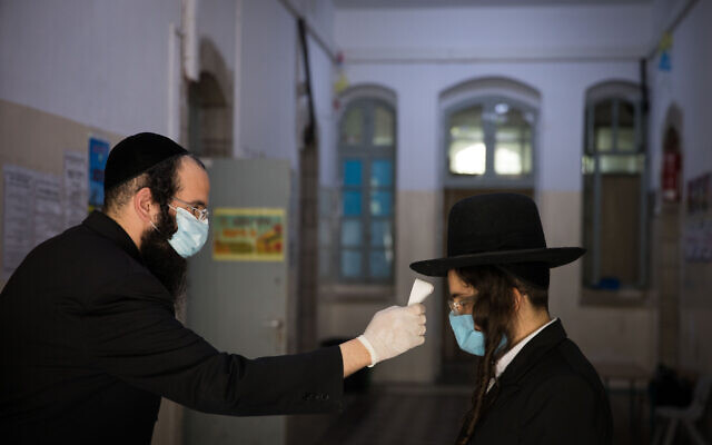 Illustrative: A teacher checks the temperature of a student to identify if he has fever at the entrance to at an ultra-Orthodox school in Jerusalem on May 6, 2020. (Nati Shohat/Flash90)