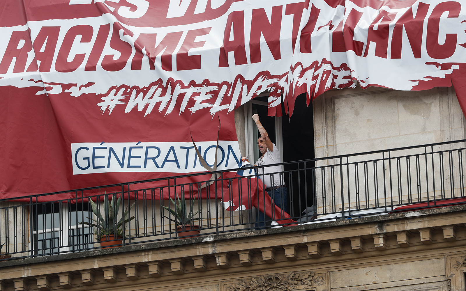 A Paris resident clenches his fist after cutting up a banner with was lowered from the roof of his building by far-right protestors, June 13, 2020. (AP/Thibault Camus)
