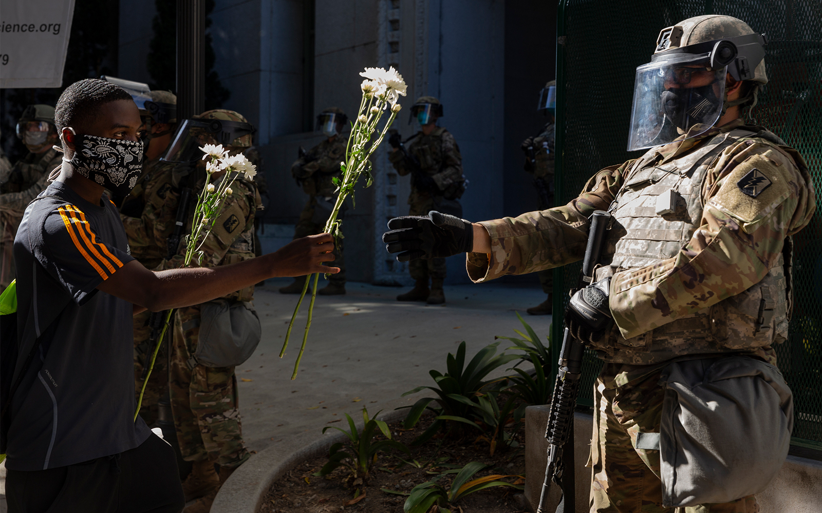 A demonstrator offers flowers to a National Guardsman stationed outside the office of Los Angeles County District Attorney Jackie Lacey, June 3, 2020, in Los Angeles, during a protest over the death of George Floyd. (AP/Damian Dovarganes)