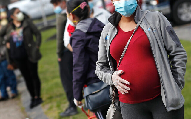A pregnant woman wearing a face mask and gloves holds her belly as she waits in line for groceries in Waltham, Massachusetts, May 7, 2020. (AP Photo/Charles Krupa)