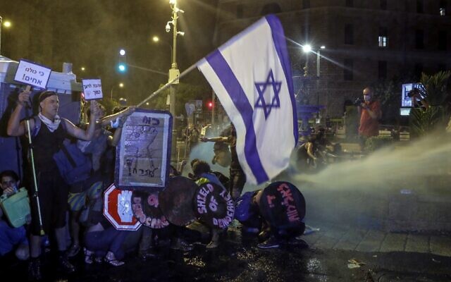 Protesters crouch down as police use water cannons against them in Jerusalem on July 25, 2020. (AHMAD GHARABLI / AFP)