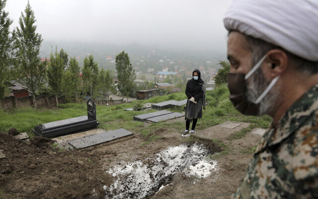 A woman wearing mask and gloves prays at the grave of her mother, who died from the novel coronavirus, at a cemetery in the outskirts of the city of Babol, in northern Iran on April 30, 2020. (AP Photo/Ebrahim Noroozi)