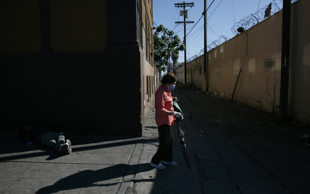 A woman with a mask and protective gloves walks past a homeless man napping on the street amid the coronavirus pandemic in the Westlake neighborhood of Los Angeles, Thursday, May 21, 2020. (AP Photo/Jae C. Hong)