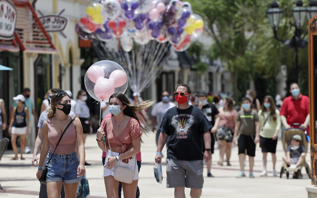 Guests required to wear masks because of the coronavirus pandemic stroll through the Disney Springs shopping, dining and entertainment complex, on June 16, 2020, in Lake Buena Vista, Florida. (AP Photo/John Raoux)