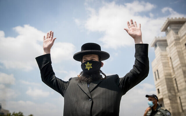 An ultra-Orthodox Jewish man wears a face mask with a yellow star on and raises his hands at a roadblock in the Hephzibah neighborhood in Beit Shemesh that is currently under a lock down in an attempt to prevent the spread of the Coronavirus, on July 10, 2020.  (Yonatan Sindel/Flash90)