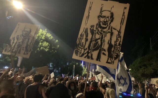 Demonstrators calling for the ouster of Prime Minister Benjamin Netanyahu hold placards showing him behind bars, in Jerusalem on July 18, 2020 (ToI staff)