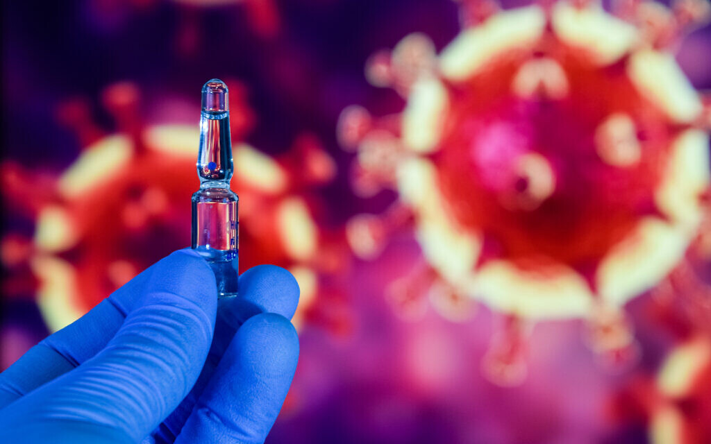 Coronavirus vaccine. A hand in medical gloves holds a vaccine and a syringe against the background of the image of the novel coronavirus. (iStock)
