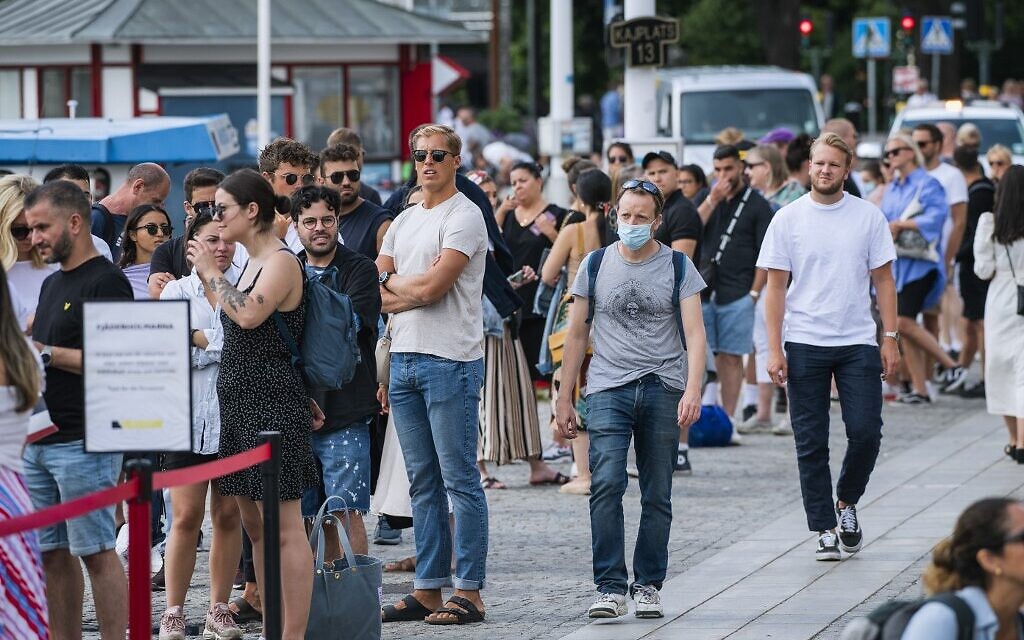 A man wearing a protective mask walks next to travelers as they queue up to board a boat at Stranvagen in Stockholm on July 27, 2020, during the novel coronavirus / COVID-19 pandemic. (Jonathan NACKSTRAND / AFP)